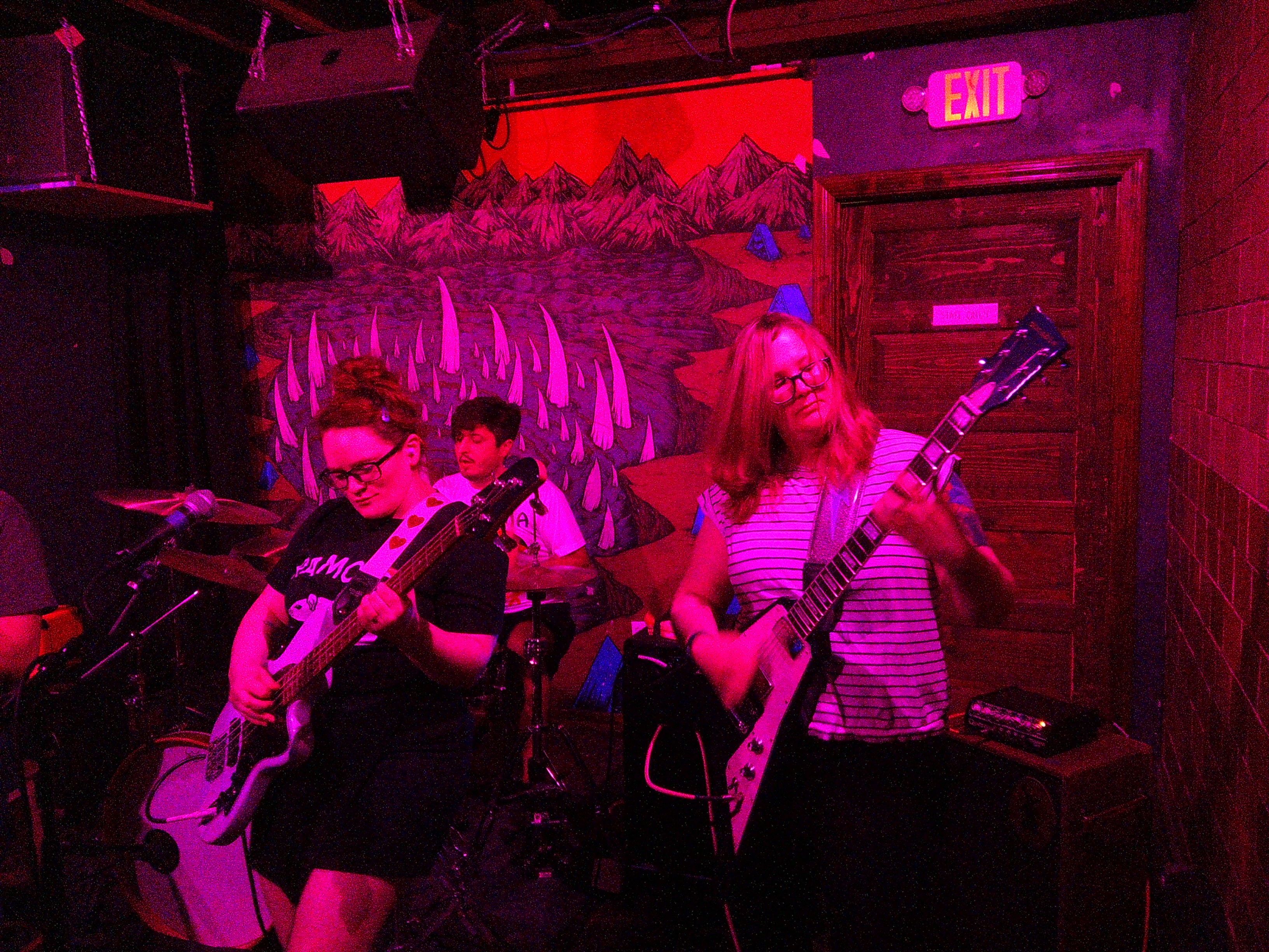 Haley playing bass and Lindsay playing guitar with Adam in the background playing drums